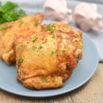garlic honey ninja foodi chicken thighs on a plate on a board next to a towel and some elephant salt and pepper shakers that are white