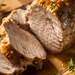 pork tenderloin sliced on a board with fresh herbs