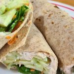 A healthy tuna wrap featuring whole wheat wraps filled with sliced cucumbers, greens, and a creamy spread on a plate.