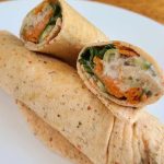 Two halved tuna wraps filled with mixed vegetables and cheese are stacked on a white plate, cleverly crafted without tortillas for a fresh, fulfilling bite.