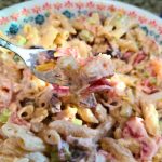 A fork holds a bite of penne pasta salad mixed with diced vegetables and a creamy ranch dressing, reminiscent of a classic Ranch Tuna Pasta Salad, all served in a floral-patterned bowl.