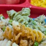 Close-up of a divided tray with tri-color rotini pasta, peas, and breadcrumbs reminiscent of a Dairy Free Tuna Casserole, plus watermelon cubes and a serving of corn.