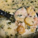 A ladle scoops creamy Loaded Zuppa Toscana Soup with potatoes, ground meat, beans, and chopped greens from a pot.