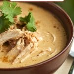 A bowl of White Chicken Chili topped with shredded chicken and fresh cilantro, with a spoon beside the bowl.