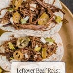 Two tacos filled with tender leftover beef roast, sliced jalapeños, chopped onions, and cilantro sit on a gold plate, with a halved lemon in the background. Text reads "Leftover Beef Roast Tacos.