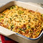 A crustless tuna quiche baked to perfection, its golden-brown top showcasing vibrant green and pink ingredients, rests invitingly on a speckled countertop.